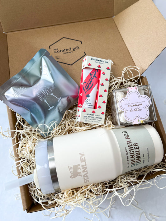 Gift box with a Stanley tumbler, candy, lip balm, and drink glitter bomb on a light background